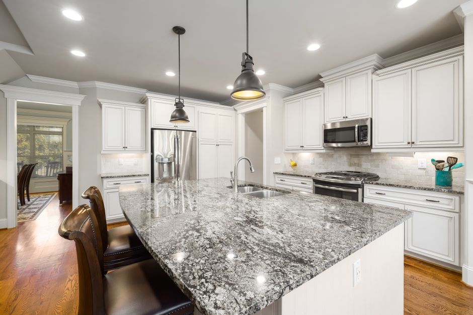 Spacious modern kitchen featuring white cabinets, granite island, and stainless steel appliances.
