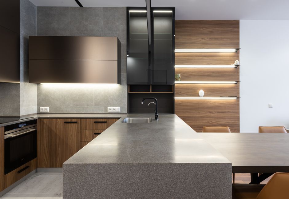 Wooden cupboards with stove placed near gray counter in modern kitchen with light decoration on wall and table in apartment